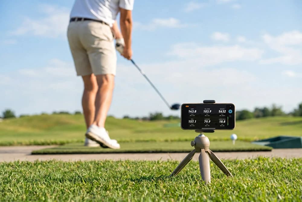 Player swinging while iPhone tracks shots and a laptop runs the game