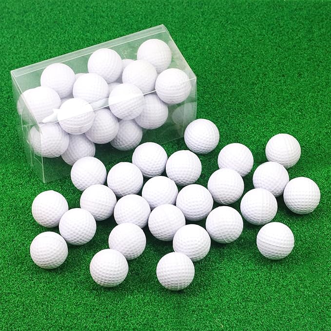 White foam practice golf balls spilling out of a clear box onto green artificial turf